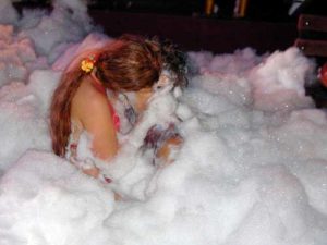 2 ladies kissing covered in foam in a foam pit