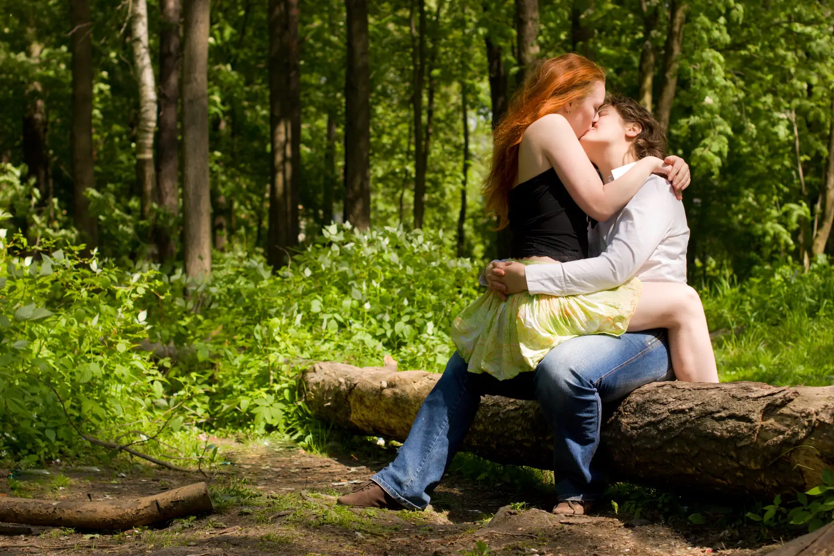 a couple sitting on a log and kissing outside