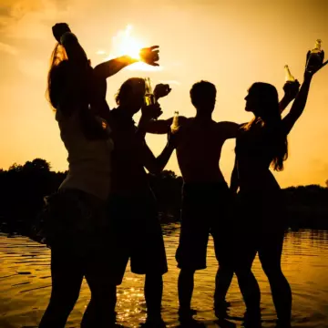 2 couples standing in water on a beach at dusk