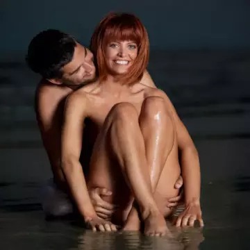 Nude couple sitting in the surf of the beach at sunset
