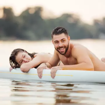 nude couple swimming on a lake surrounded by a forest